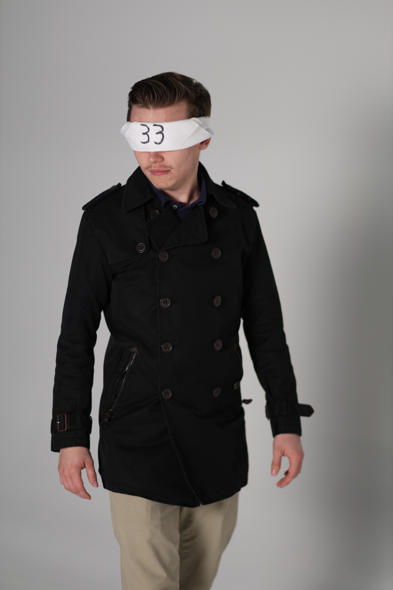 Blindfolded figure wearing black coat with 33 over the eyes