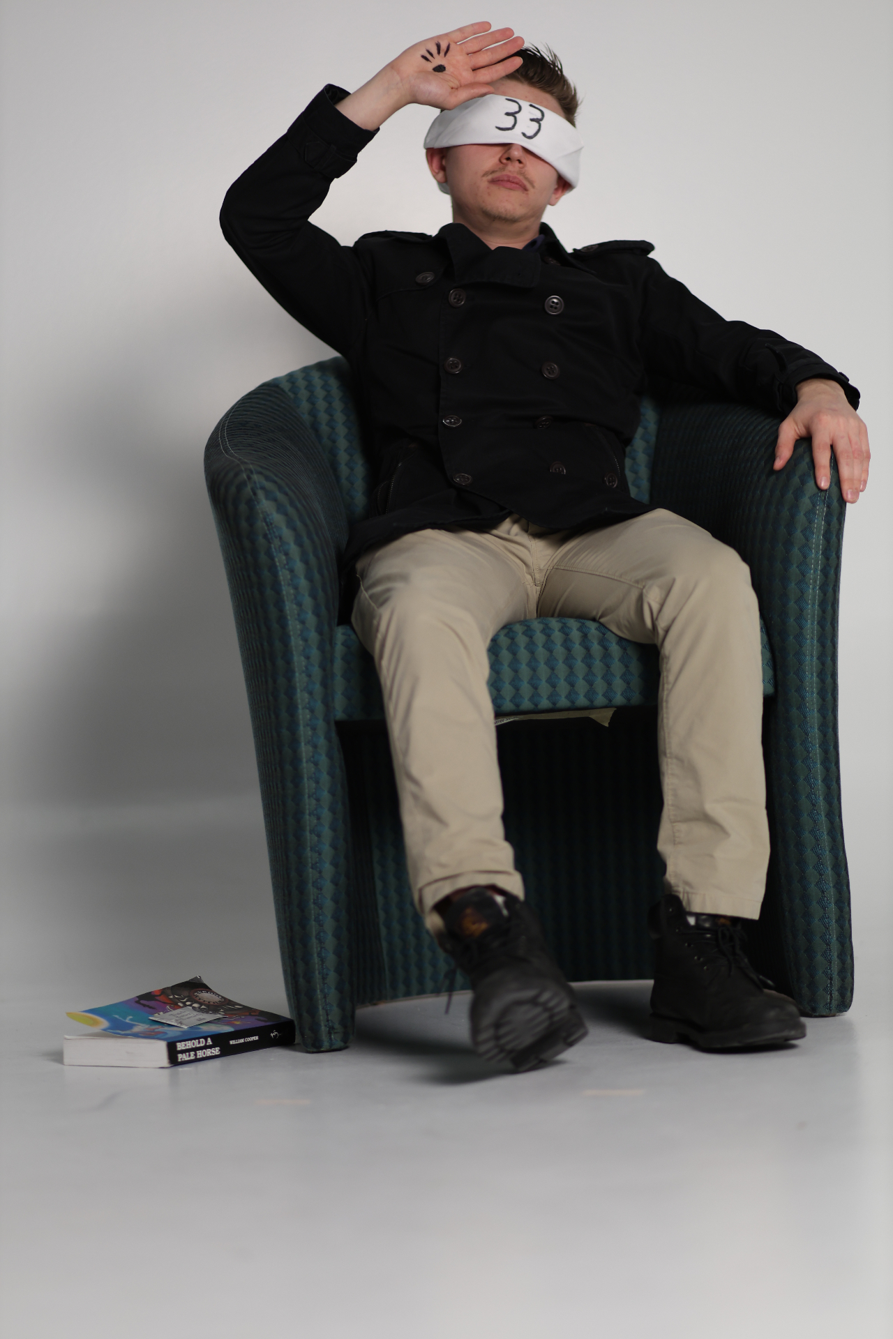 Blindfolded figure seated in a chair with hand raised
